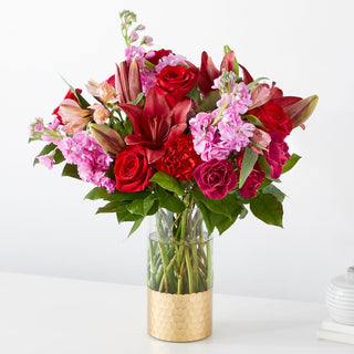 red lilies, red roses, pink stocks, carnations in a beautiful gold vase.