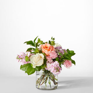 Pastel flower arrangement with peach and white roses, blush pink stock, and billy balls in a clear glass vase — romantic spring bouquet Toronto florist.