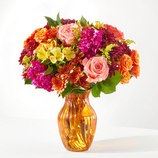 Autumn flower bouquet with orange roses, coral pink blooms, chrysanthemums, and fuchsia stock in an amber vase — fall flowers Toronto florist