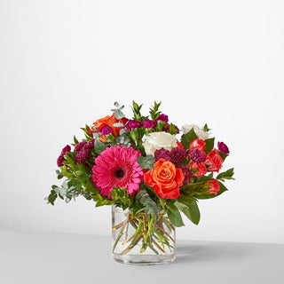 Vibrant mixed-color flower bouquet with hot pink gerberas, orange roses, white roses, and carnations arranged in a clear glass vase — luxury floral gift from Yunza Florist Toronto