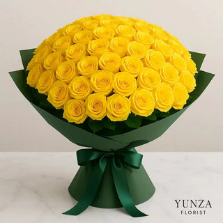 Elegant 100 yellow roses bouquet wrapped in matte green paper with satin ribbon, arranged in a dome shape on a white marble table — luxury floral arrangement by Yunza Florist Toronto