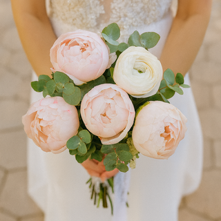 Elegant bridal bouquet with blush pink and white peonies accented with eucalyptus greenery, held by a bride in a white dress. Perfect for weddings and special occasions.