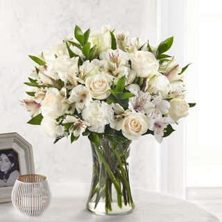 Fresh white roses and carnations arranged in a clear vase for funeral or home sympathy display
