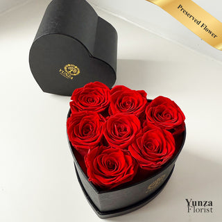 Heart-shaped box of red preserved roses with a black lid on a white background, branded 'Yunza Florist'.