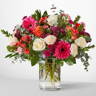 Mixed-color flower bouquet in clear vase with pink gerbera daisies, coral roses, white roses, and lush greenery — designed by Yunza Florist Toronto.
