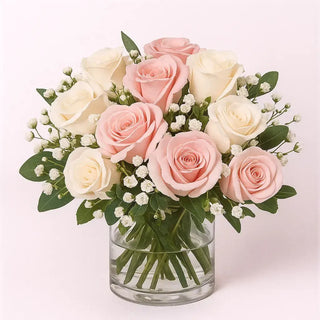 Elegant centerpiece of pink and white roses with baby's breath in a clear glass vase on a white background.
