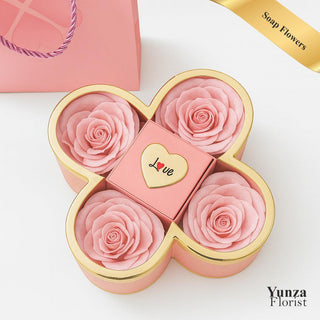 Yunza Florist Clover Soap Rose Box featuring four large pink soap flowers and a central square compartment with a heart and the word "LOVE," accented with gold trim.