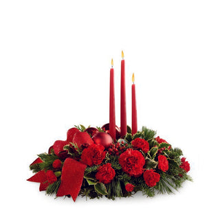 Red and green Christmas table centerpiece decorated with candles, ribbon, and pine cone